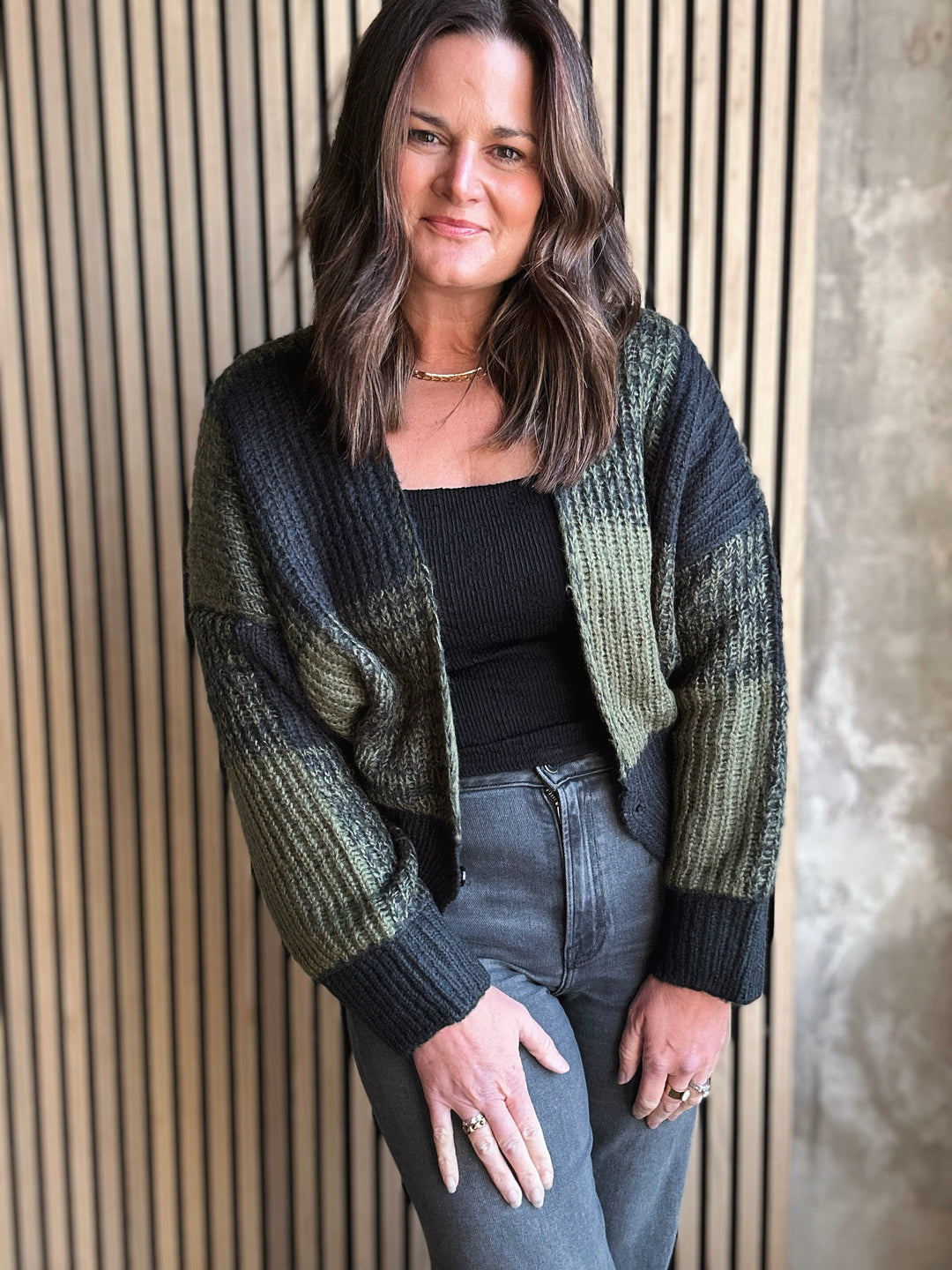 Woman wearing a green and black cardigan against a wooden paneled wall.