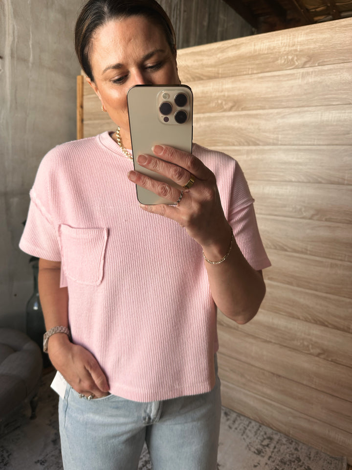 A woman wearing a textured light pink short sleeved shirt with a pocket on the left side of the shirt. 