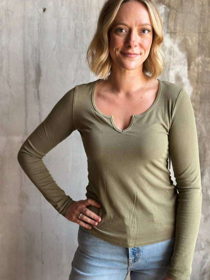 Woman wearing a green long-sleeve top against a textured wall.