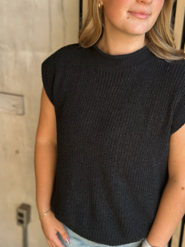 Person wearing a black ribbed knit sleeveless top against a neutral background