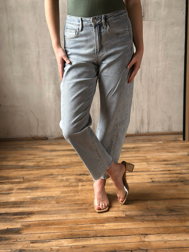 Person wearing light blue jeans standing on a wooden floor with a neutral wall background
