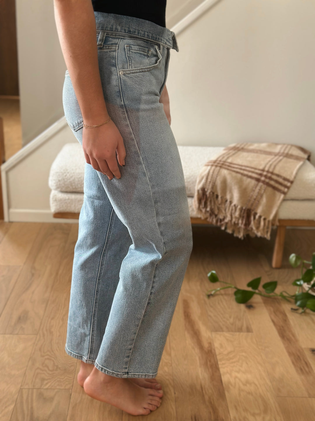 Person wearing light blue jeans standing on a wooden floor with a couch and blanket in the background.