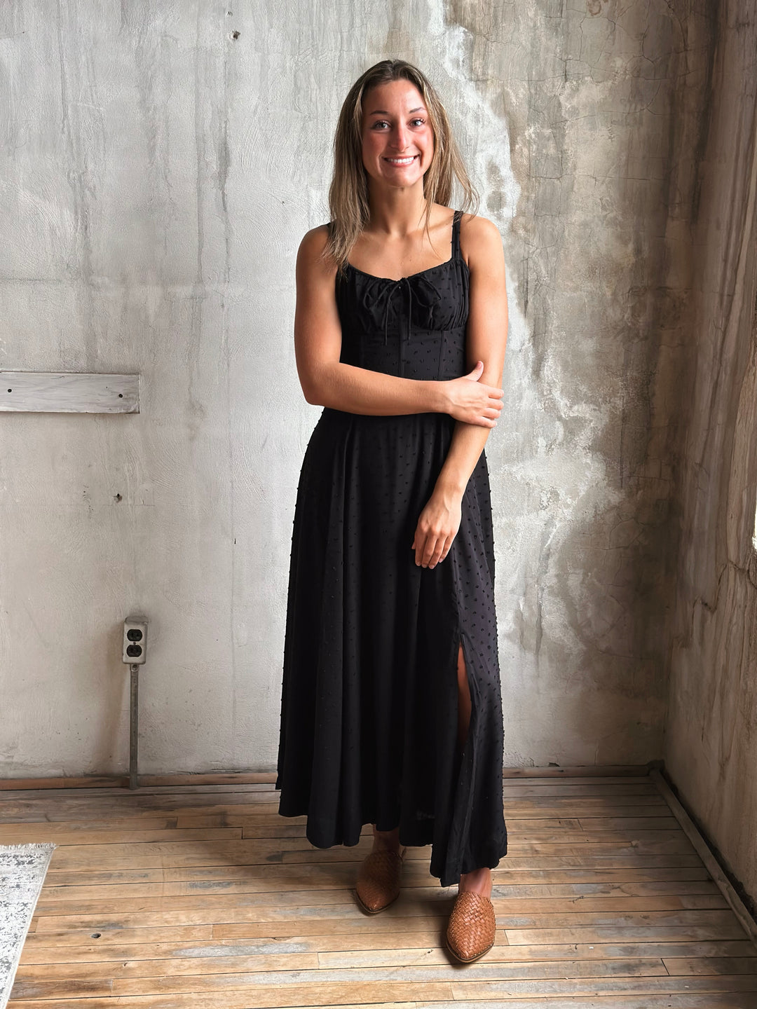 Woman wearing a black dress standing against a textured wall.