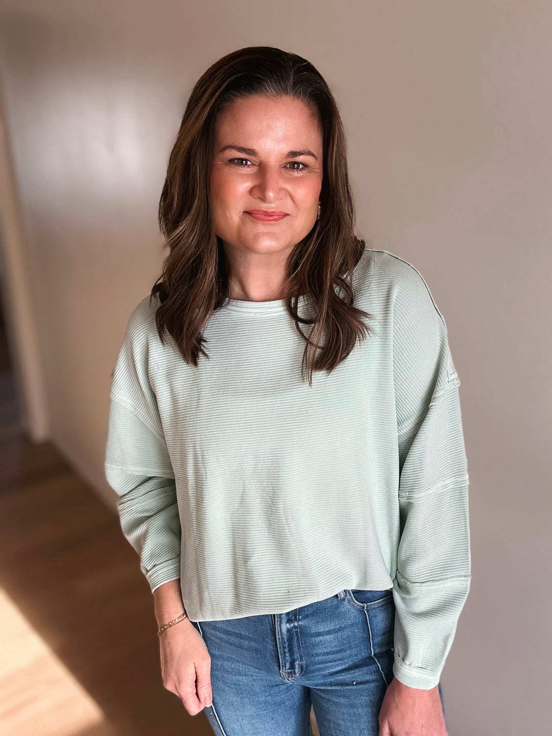 Woman wearing a light green sweater and blue jeans indoors.