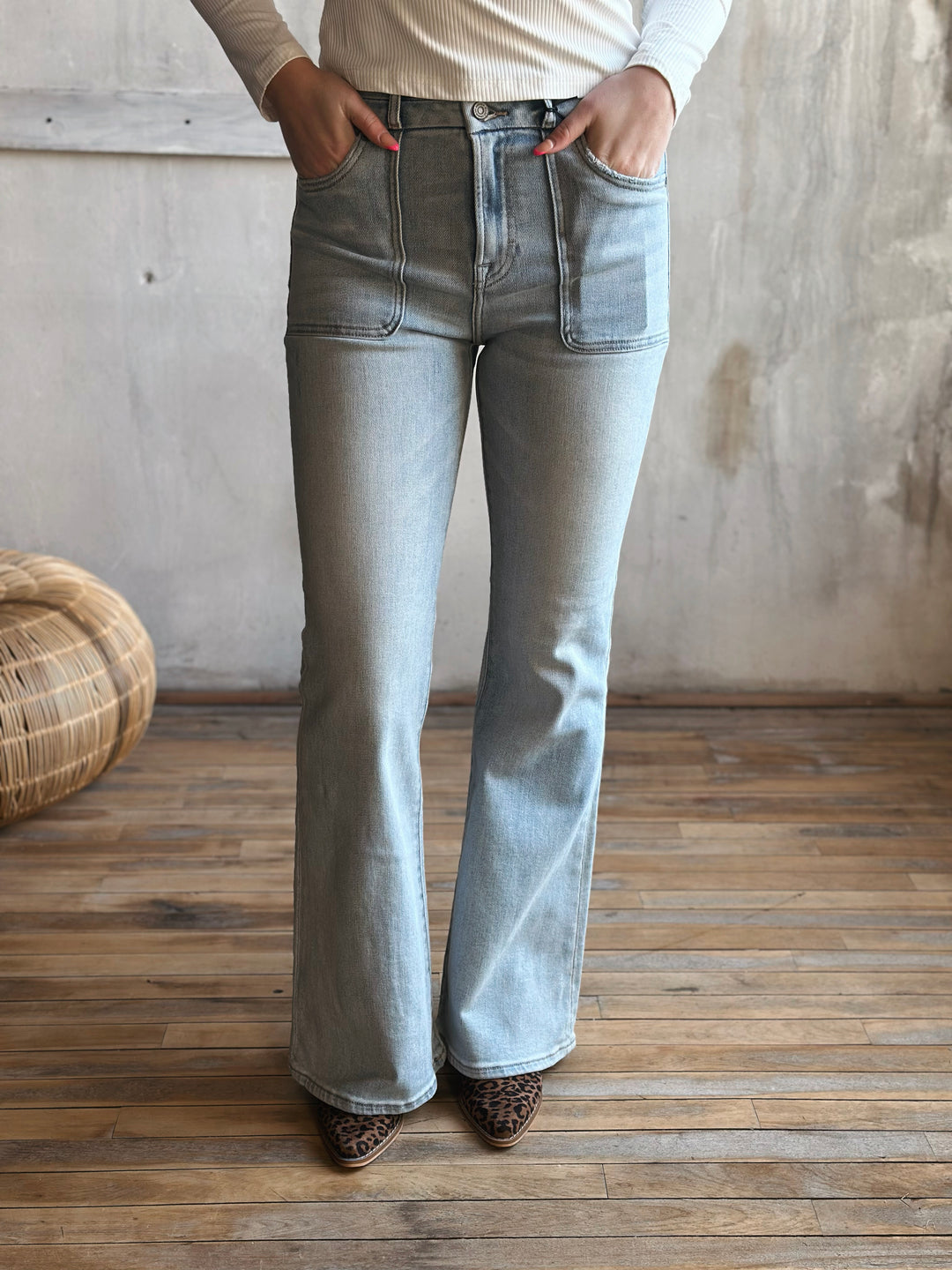 Person wearing light blue flared jeans standing in a room with wooden floor and textured wall.