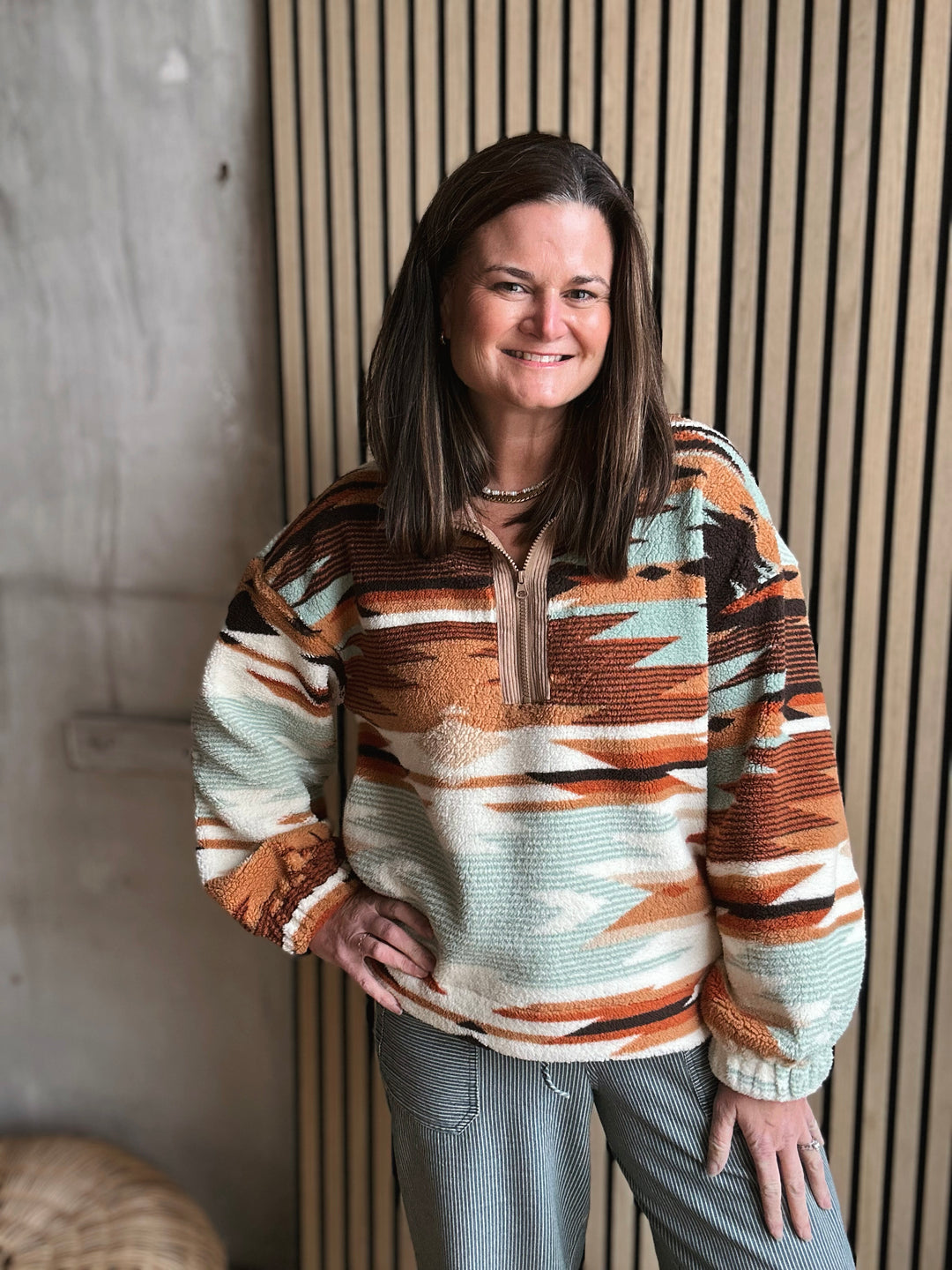 Woman wearing a patterned sweater standing against a neutral wall.