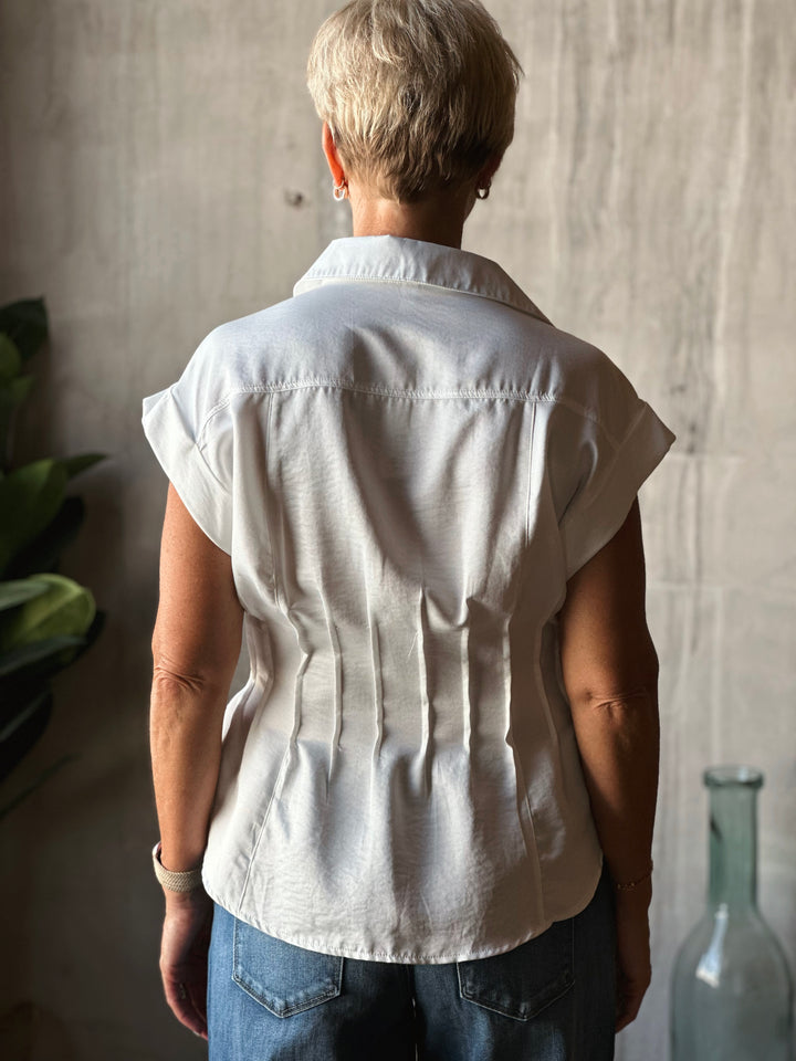 Person wearing a white sleeveless shirt against a neutral wall.
