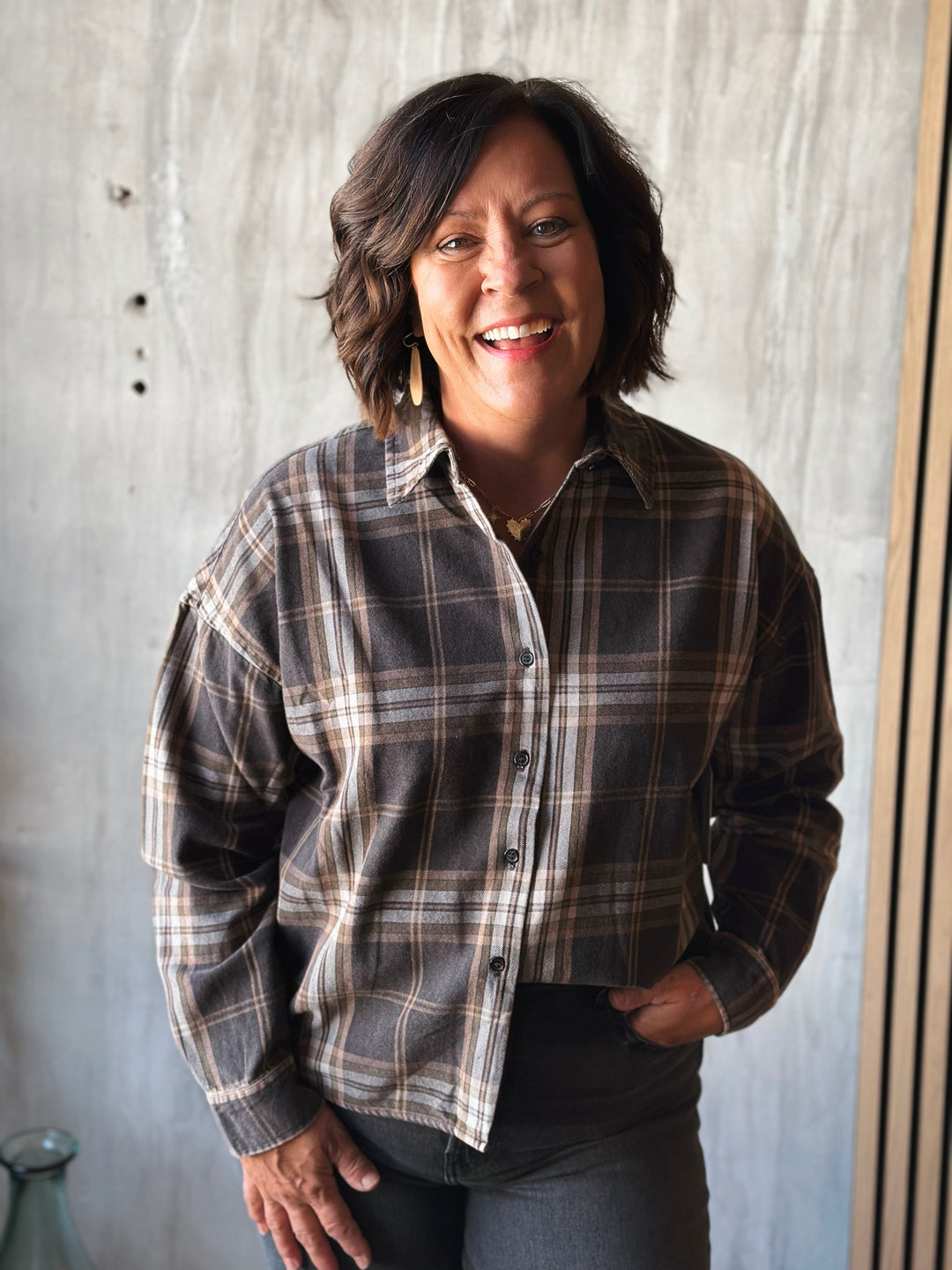 Person wearing a plaid shirt standing against a textured wall.
