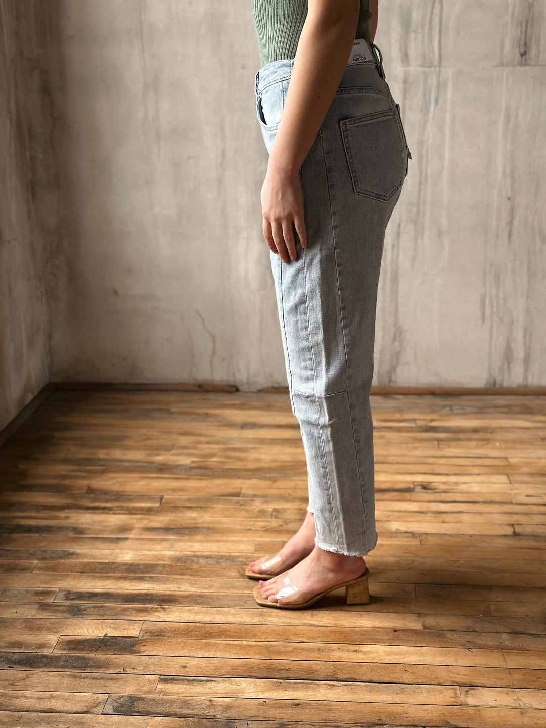 Person wearing light blue jeans standing on a wooden floor with a neutral wall background