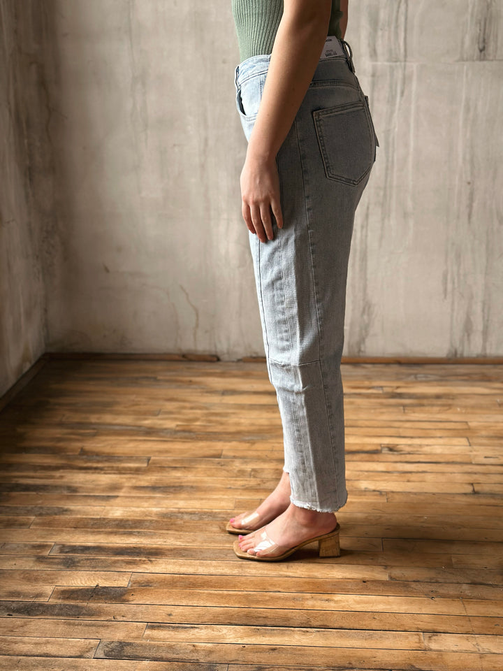 Person wearing light blue jeans standing on a wooden floor with a neutral wall background