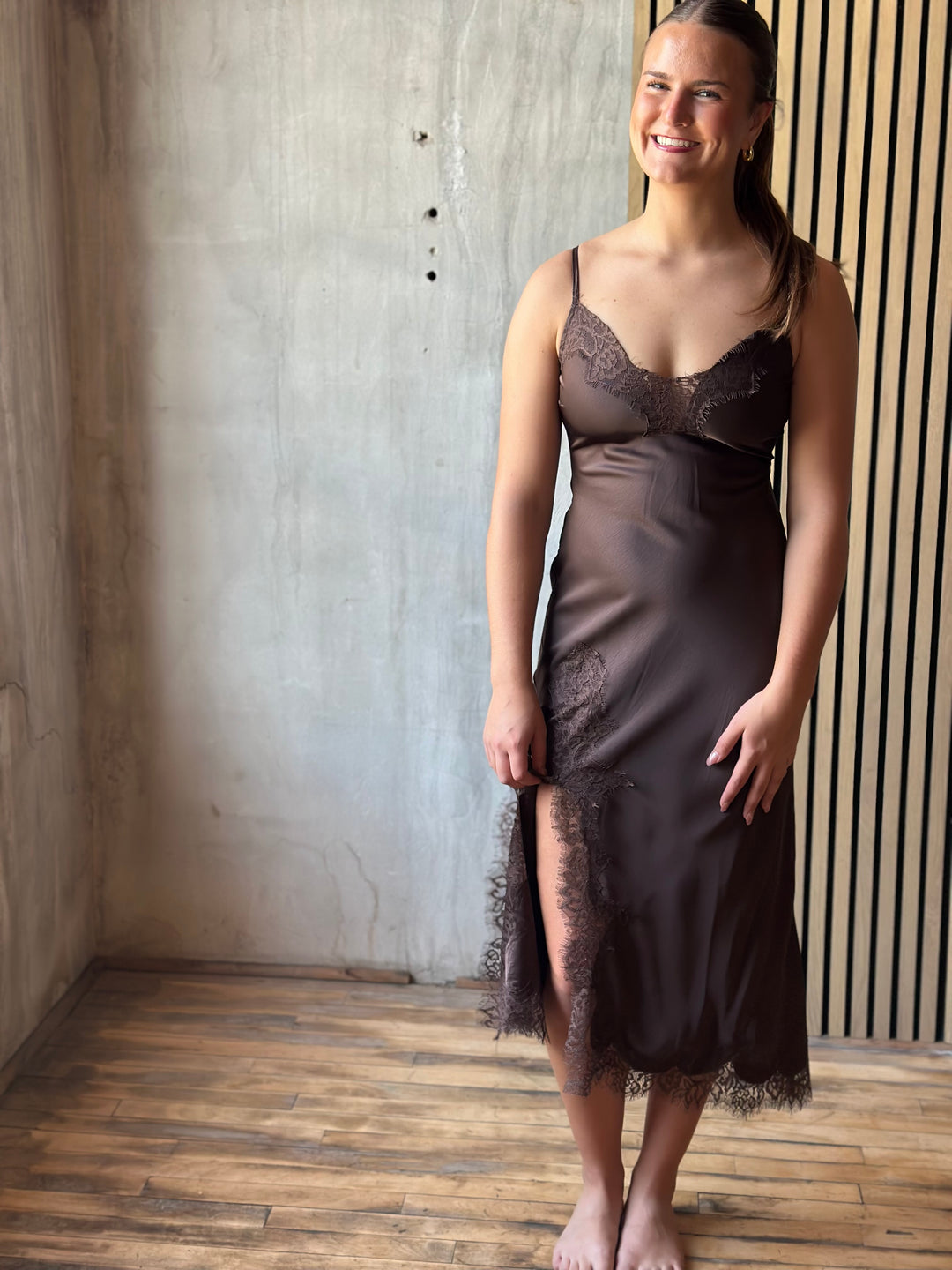 Woman wearing a chocolate brown satin slip dress with a lace-trimmed neckline and hem