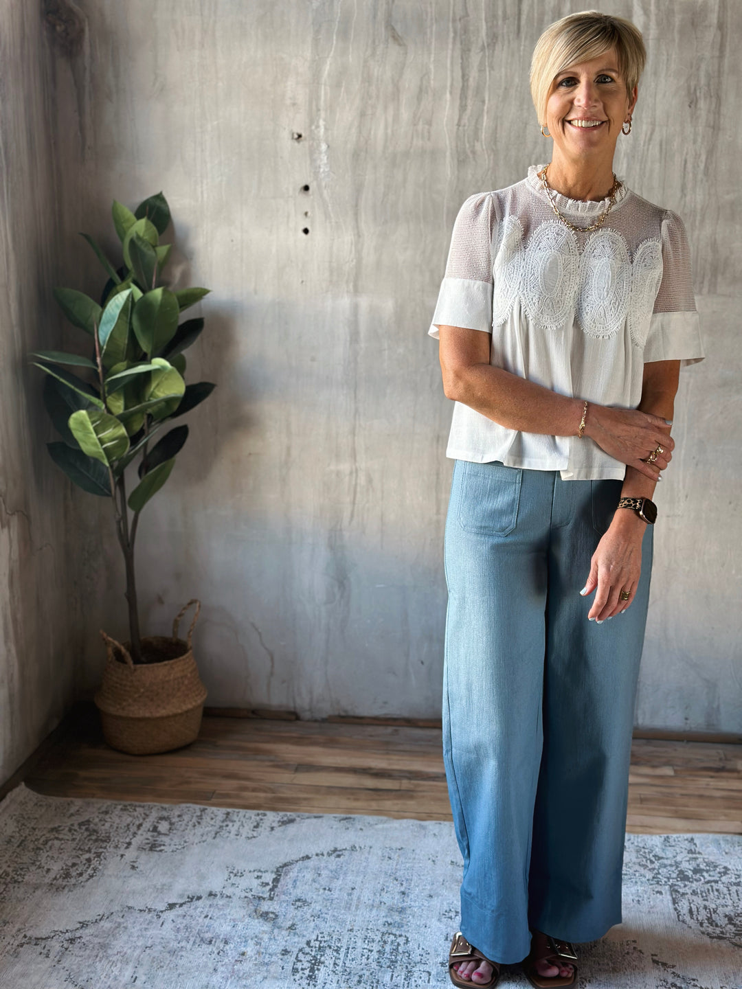 Woman standing in a room with a plant and textured wall.