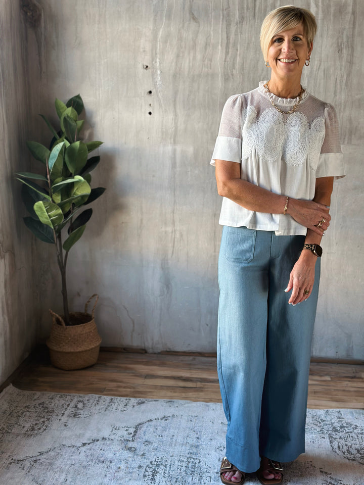 Woman standing in a room with a plant and textured wall.