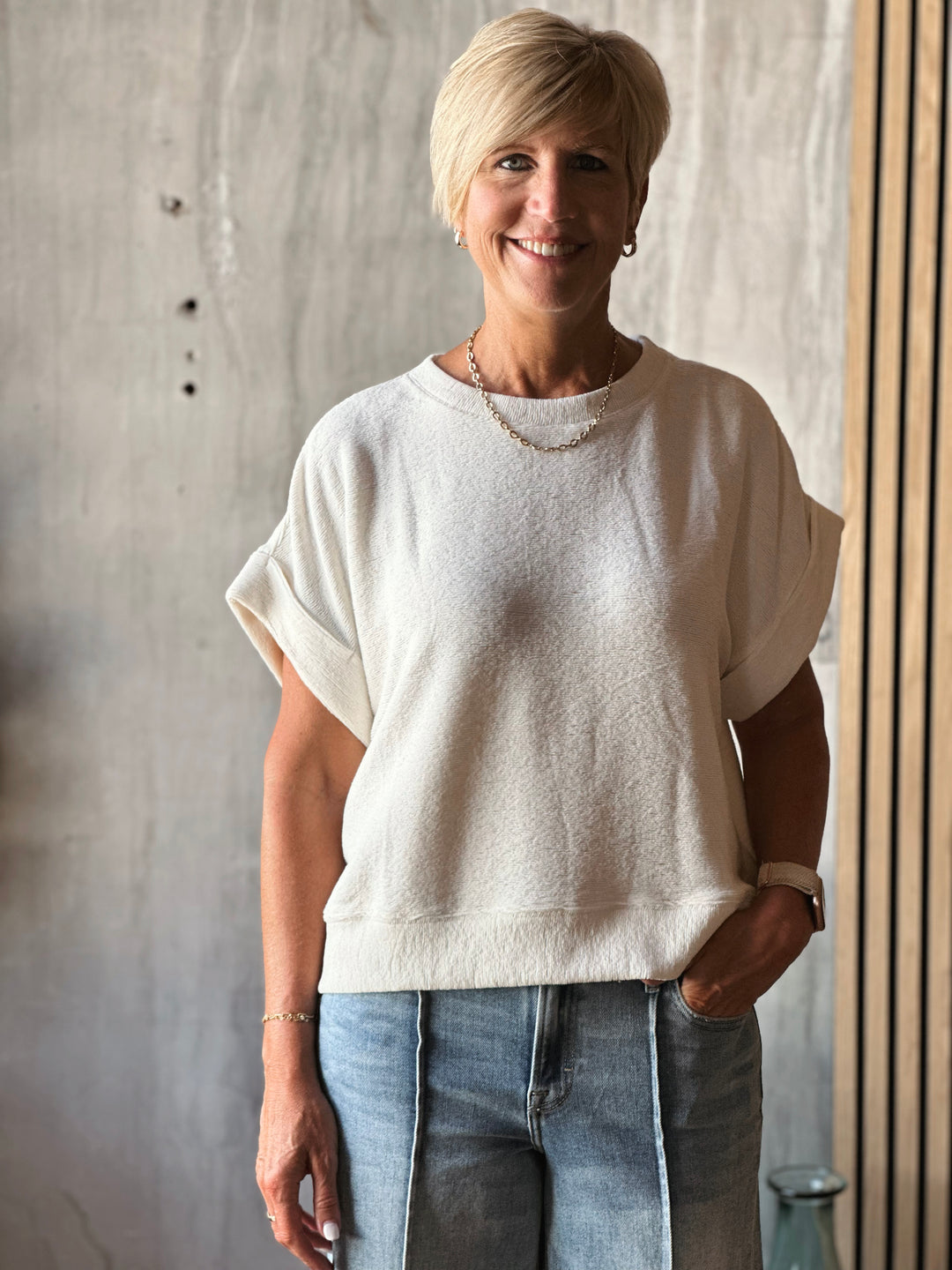 Woman wearing a white sweater and blue jeans standing against a neutral background