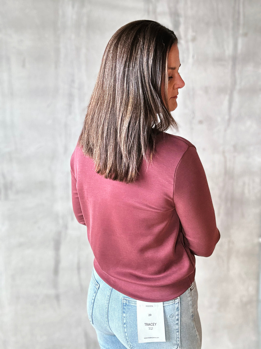 Woman wearing a pink long-sleeve top and light blue jeans against a plain background