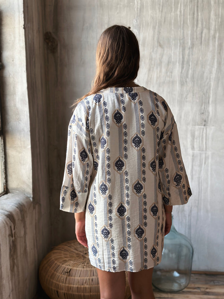 A woman wearing a patterned dress with long sleeves in a room with wooden walls and a large vase.