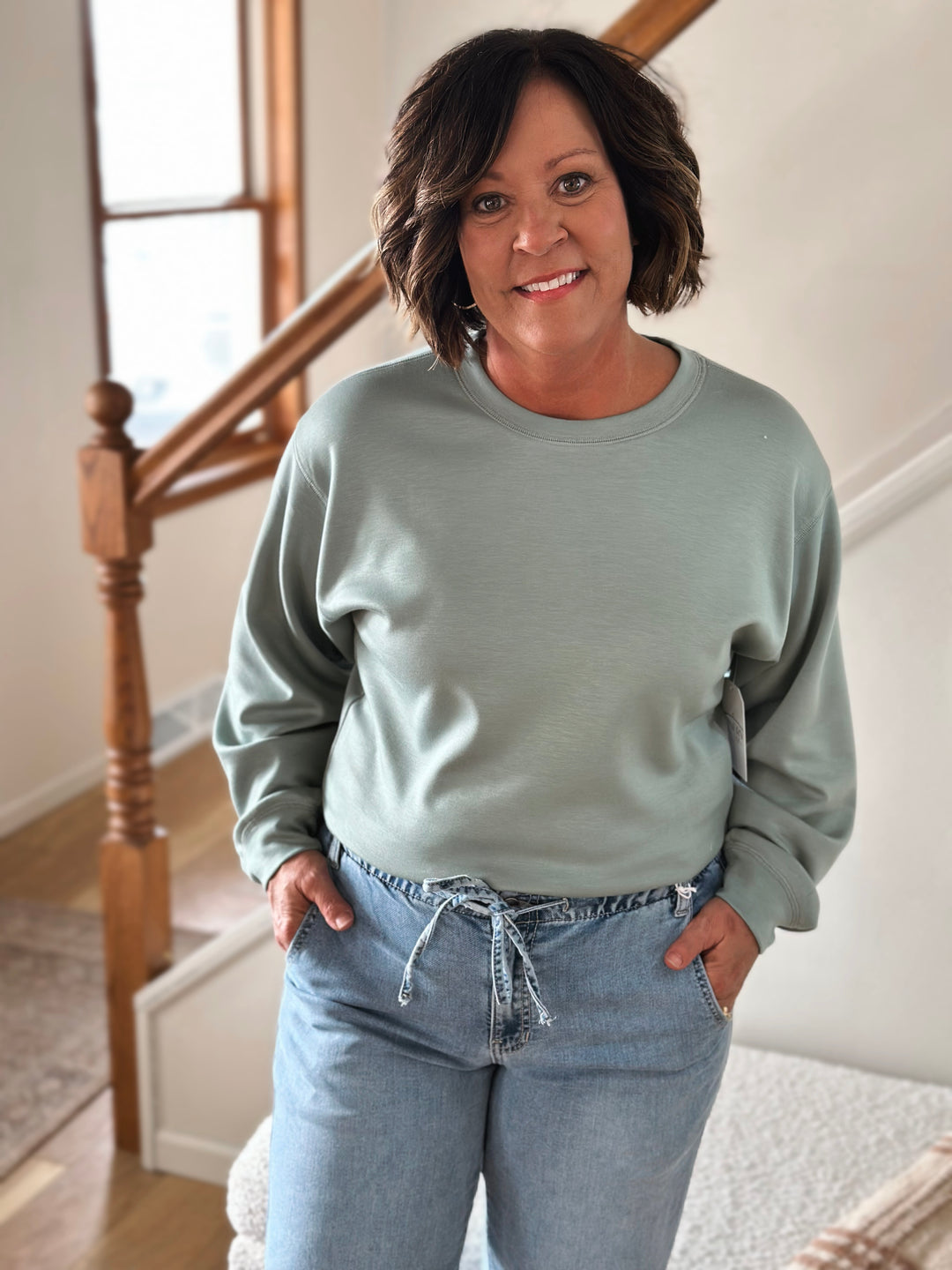 Woman wearing a light green sweater and blue jeans standing indoors.