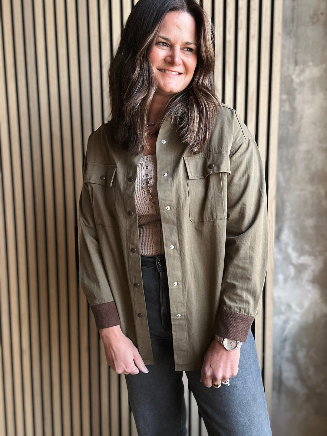 Woman wearing a green jacket standing against a striped wall.