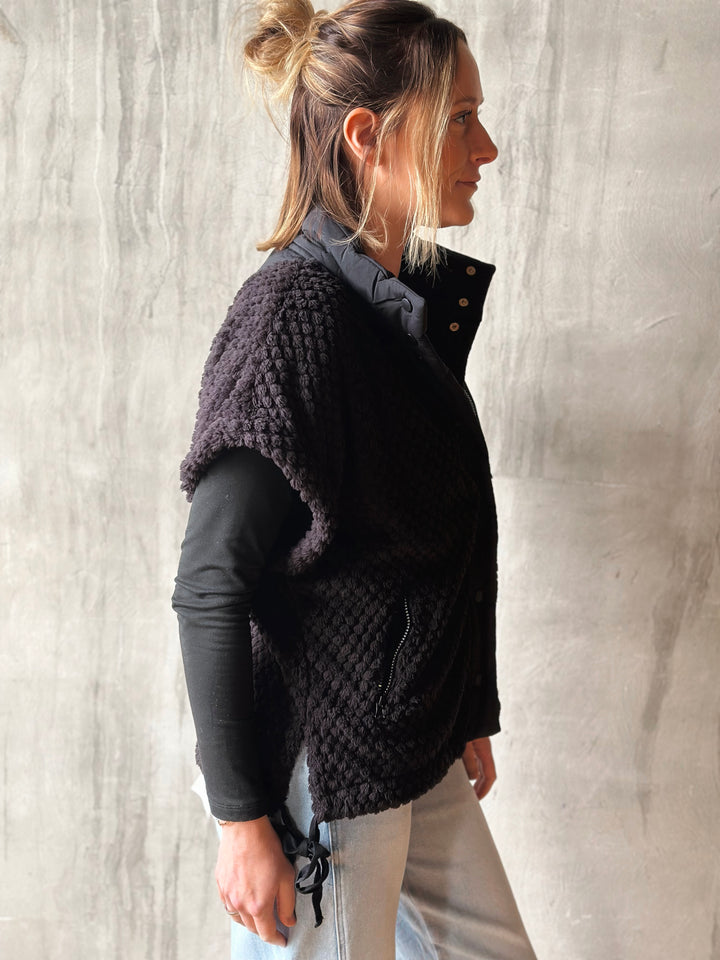 Woman wearing a black textured vest over a black shirt against a light background