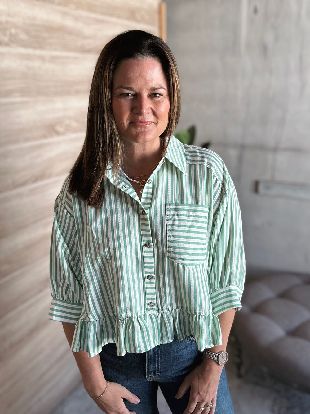 Woman wearing a green and white striped shirt with a ruffle hem at the bottom of the shirt and buttons down the middle.