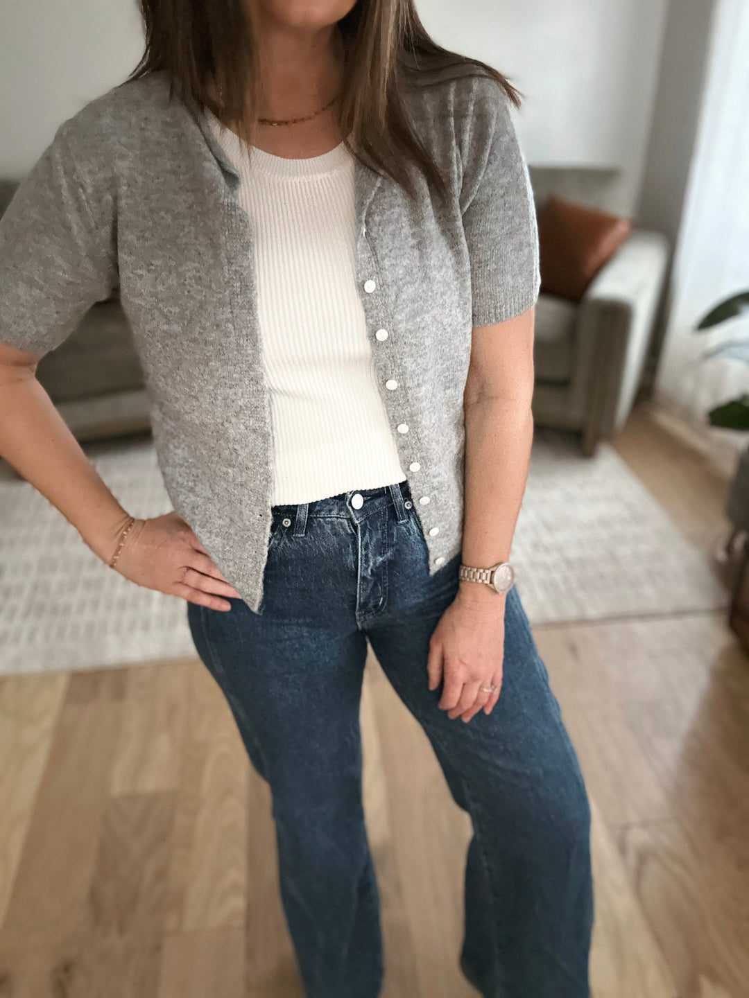 Person wearing a gray cardigan, white shirt, and blue jeans indoors.