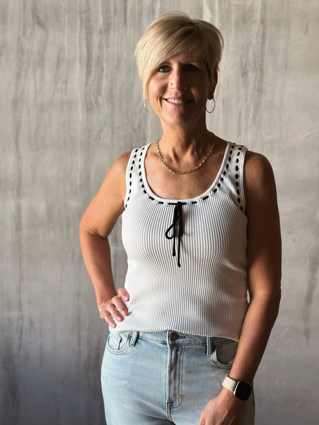 front view of sleeveless sweater knit tank features a flattering scoop neckline and a playful front tie detail. Cream top with black bow. 