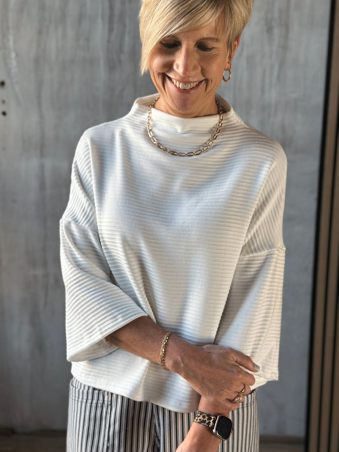 Woman wearing a light colored sweater and striped pants against a neutral background