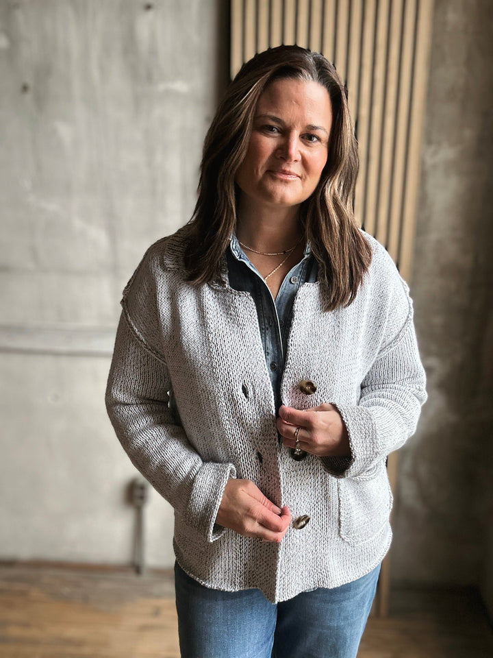Woman wearing a light gray jacket over a denim shirt in an indoor setting.