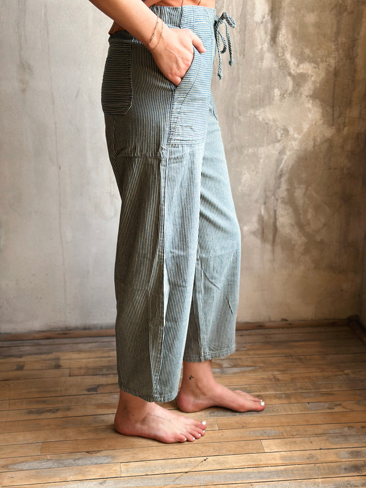 Person wearing checkered pants standing on a wooden floor with a textured wall background
