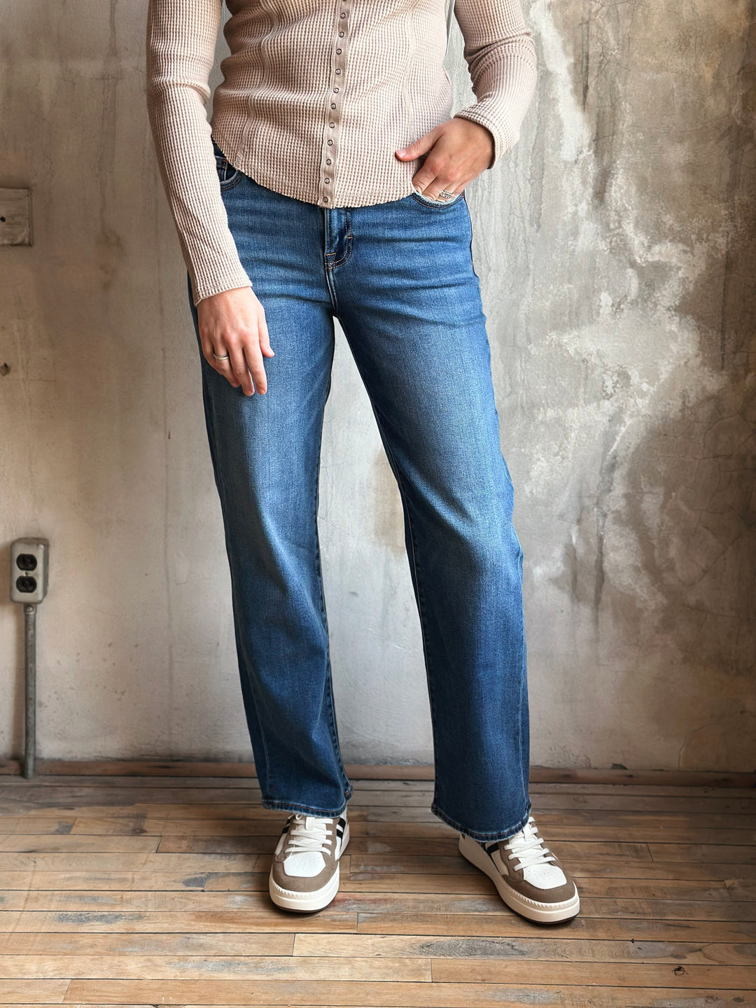 Person wearing blue jeans and a beige sweater against a textured wall.