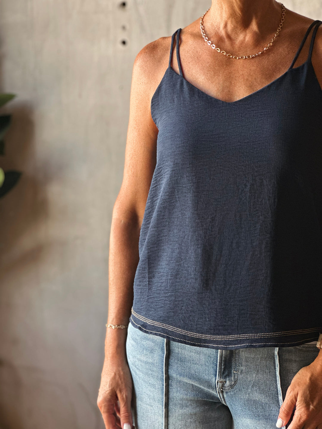 Person wearing a dark blue tank top and light blue jeans against a neutral background