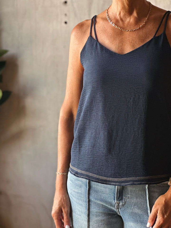 Person wearing a dark blue tank top and light blue jeans against a neutral background