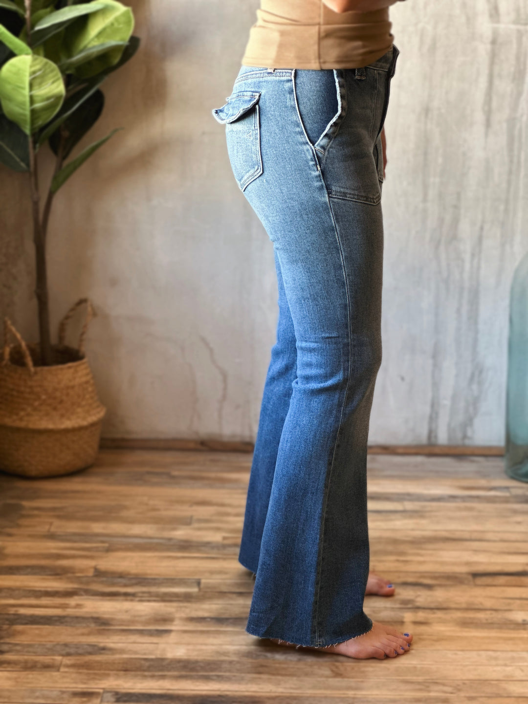 Person wearing blue flared jeans standing in a room with a plant and wooden floor.