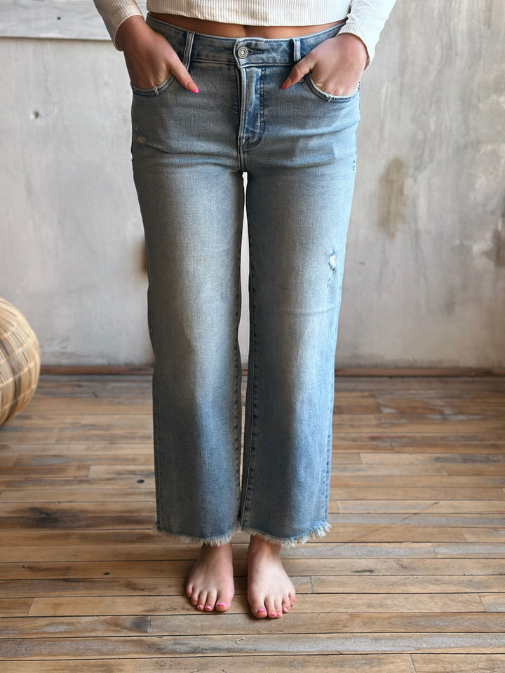Person wearing light blue jeans standing on a wooden floor with a neutral background