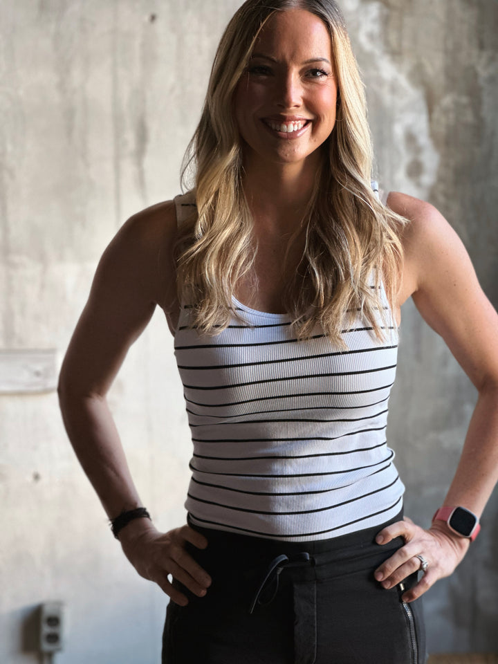 Woman wearing a striped tank top and black pants against a neutral background