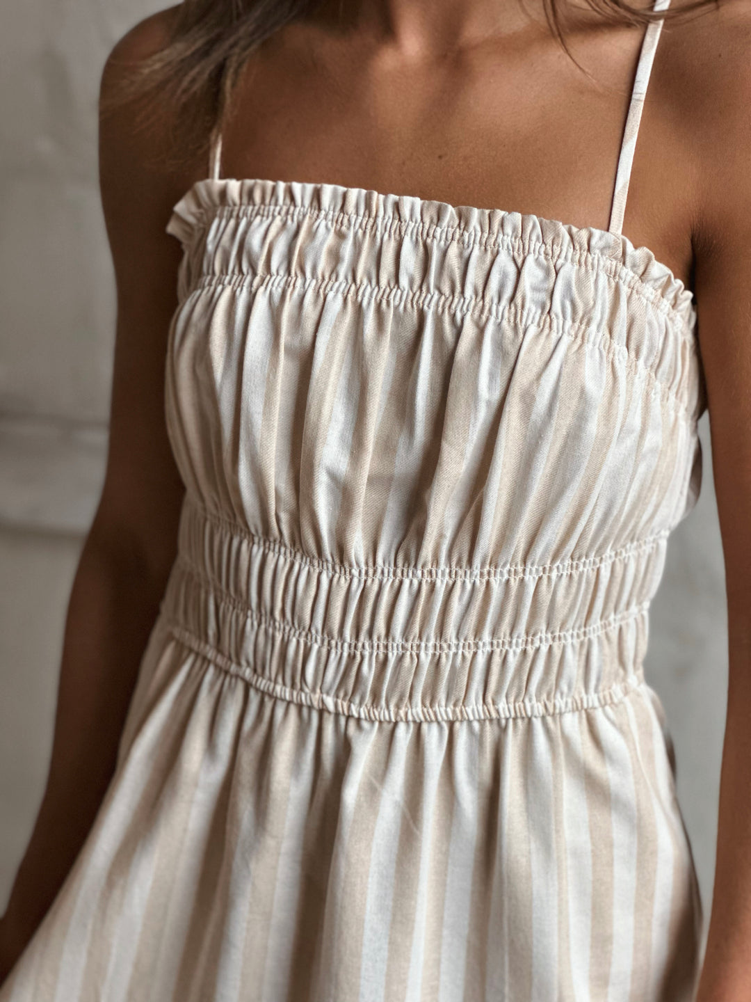 A woman wearing a white and cream striped dress against a neutral background.