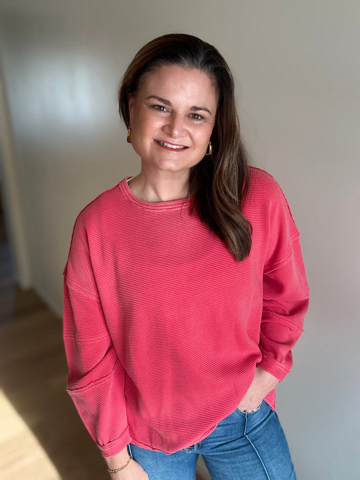 Woman wearing a pink sweater and blue jeans standing against a plain wall.