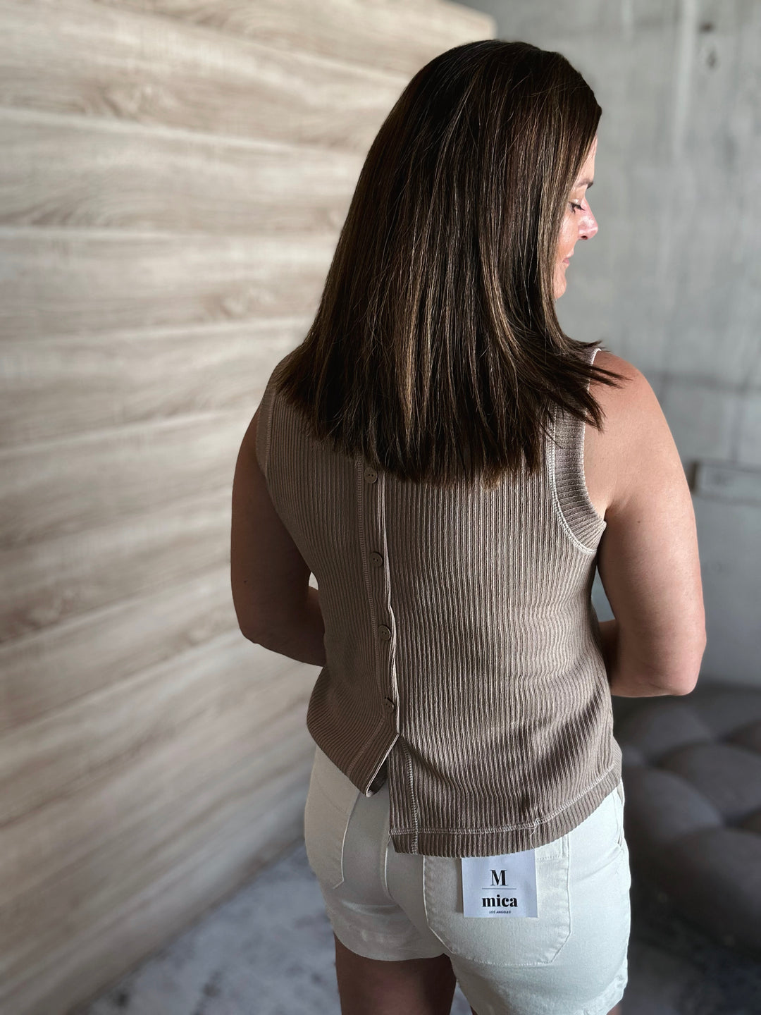 Woman wearing a beige ribbed tank top with buttons going down the middle of the shirt. 