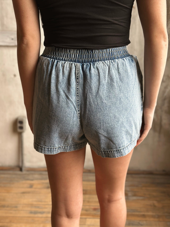 Person wearing denim shorts and a black top against a neutral background