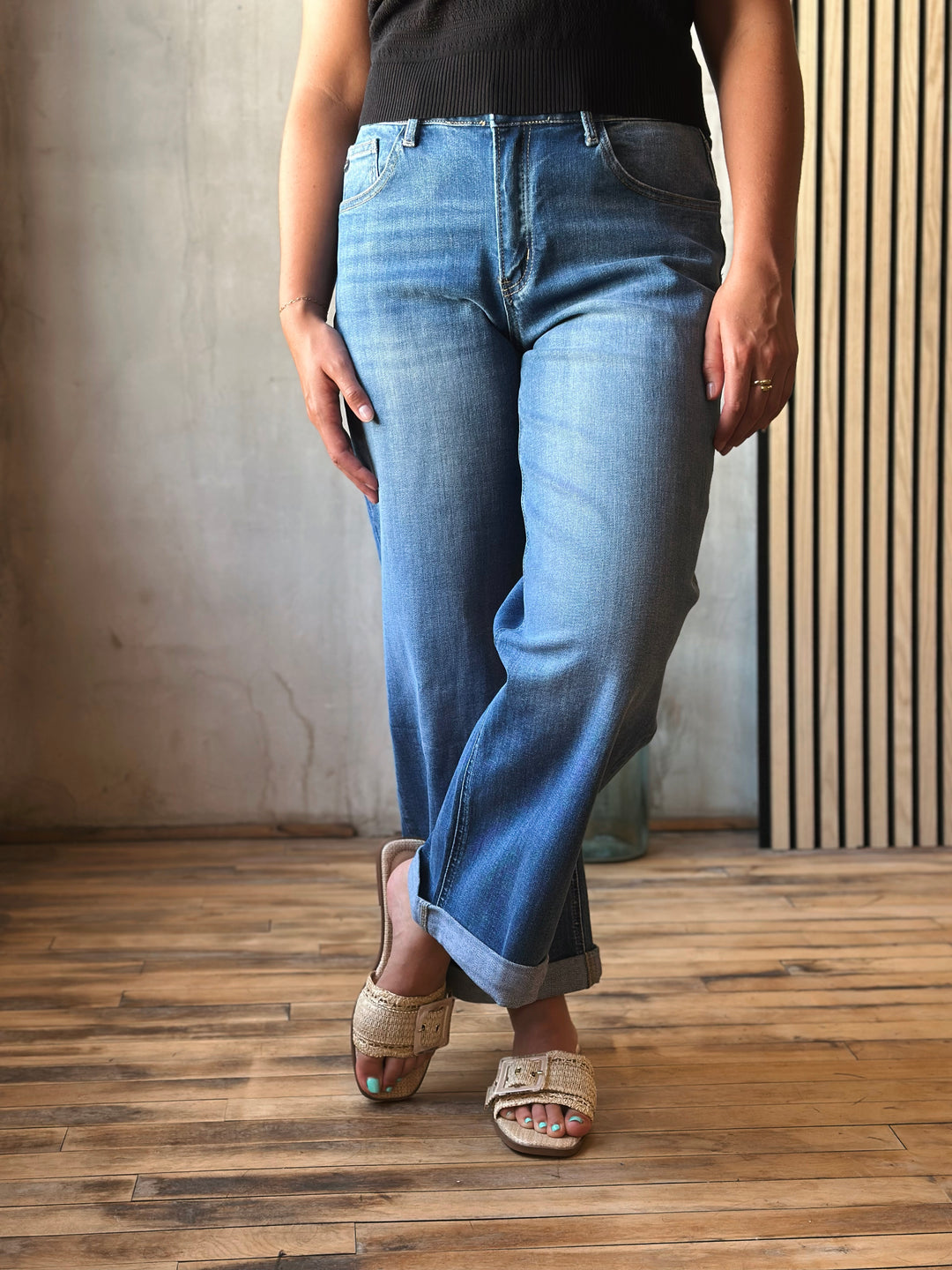 Person wearing blue jeans and sandals on a wooden floor with a neutral wall background