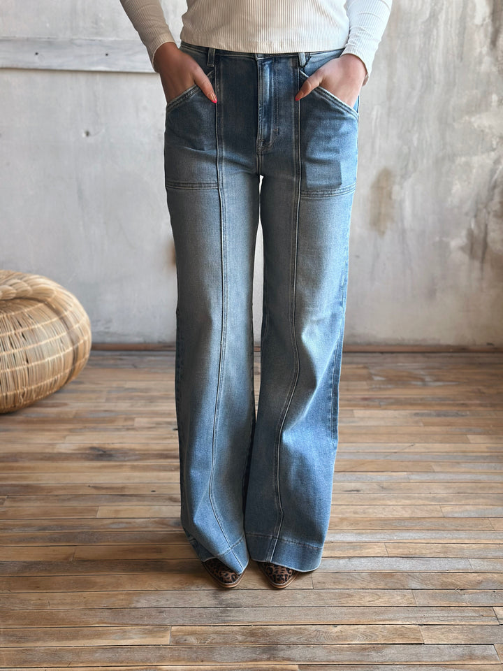A person wearing blue flared jeans standing on a wooden floor.