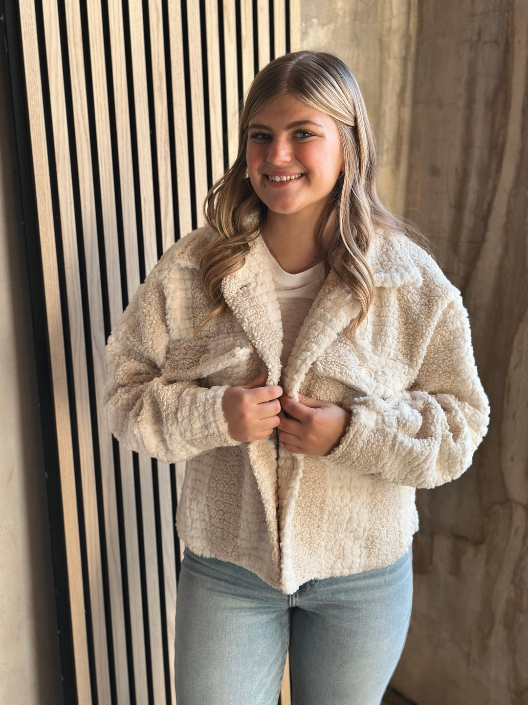 Woman wearing a beige sherpa jacket standing against a neutral background