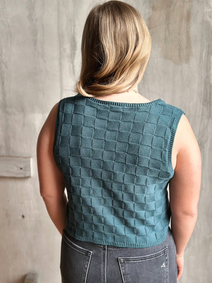 Person wearing a teal checkered vest against a neutral background
