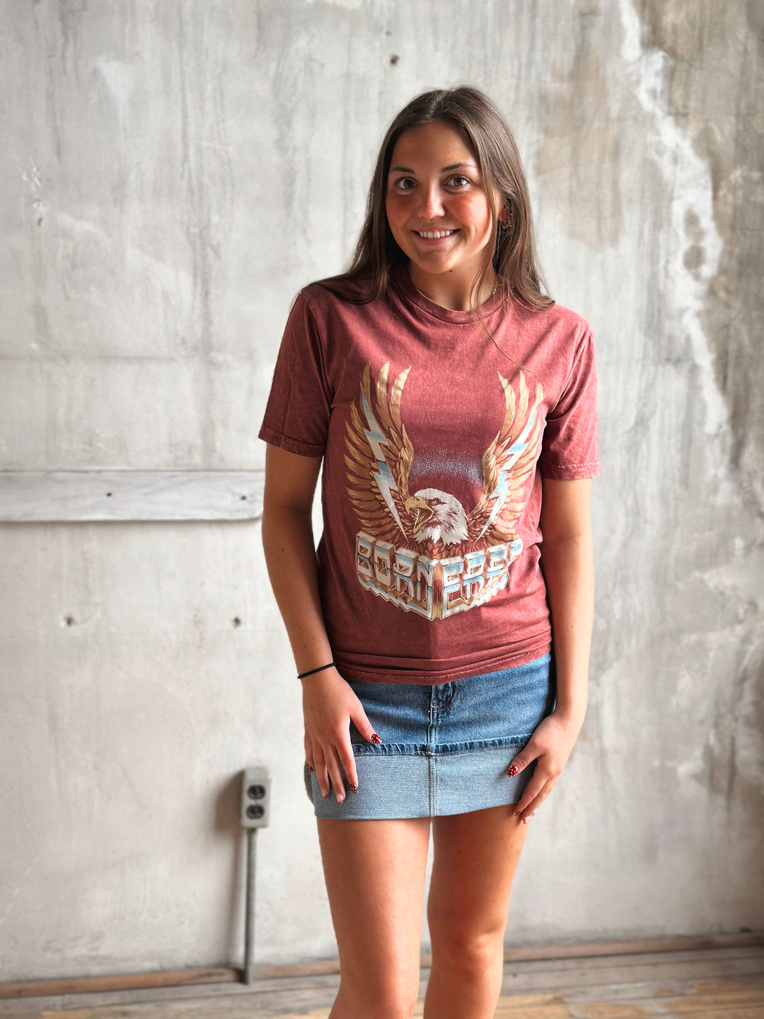 Woman wearing a red t-shirt with an eagle graphic against a textured wall.