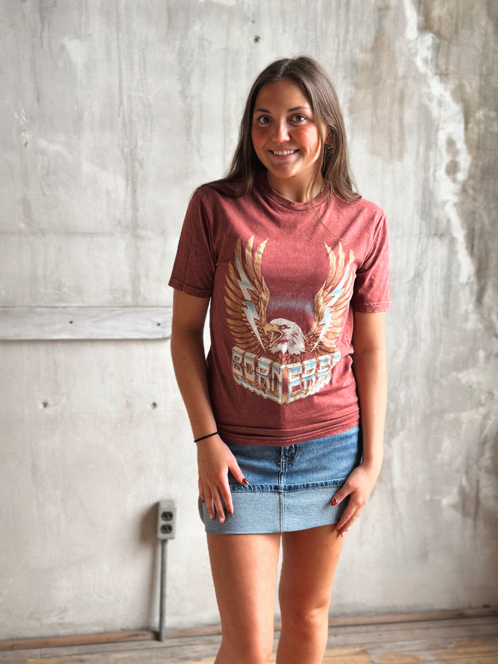 Woman wearing a red t-shirt with an eagle graphic against a textured wall.