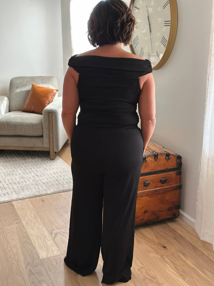 Back of person wearing a black off-shoulder top and wide-leg pants.