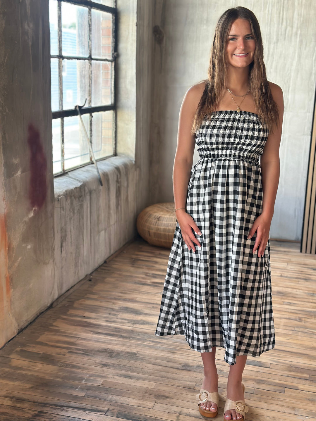 Woman wearing a black and white plaid strapless dress standing in a room with wooden floor and large window.