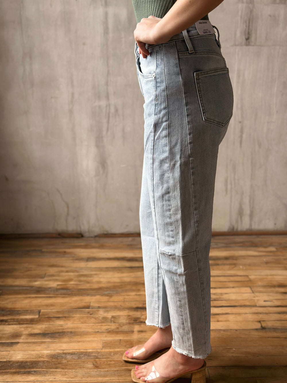Person wearing light-colored jeans standing on a wooden floor with a neutral wall background