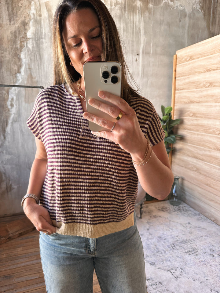 Woman wearing a beige and plum striped v-neck shirt and jeans standing indoors.