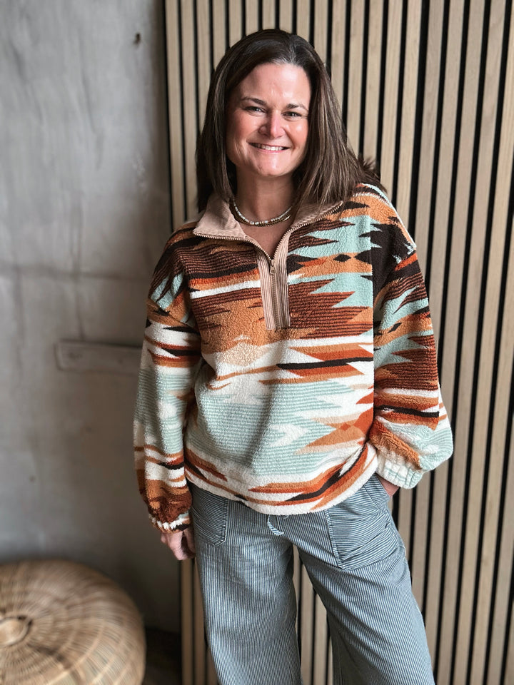 Woman wearing a patterned sweater standing against a textured wall.